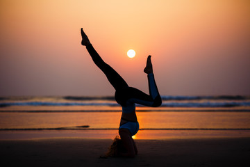 Woman practicing yoga on the beach at sunset