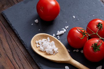 Vegetarian still life with fresh grape tomatoes, pepper and salt in wooden spoon on wooden background, selective focus