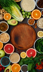 Around wooden kitchen board set clean eating. Vegetarian healthy food - different vegetables and fruits, superfood, seeds, cereal, leaf vegetable on dark background top view Flat lay
