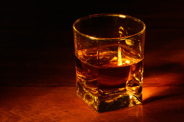 a glass of whiskey on a wooden table and a dark background