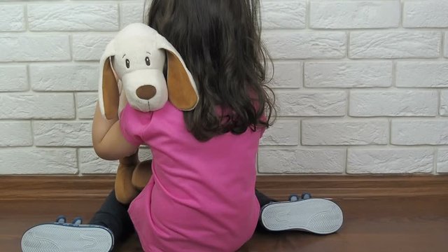 Depression of the child. A little girl is sitting on the floor and hugging a toy.