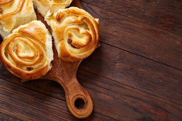 Homemade rose buns on wooden cutting board over rustic vintage background, close-up, shallow depth of field