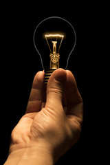 Hand holding a filament lamp on a black background. The bulb as a symbol of an idea. Glowing...