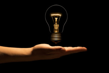 Hand holding a filament lamp on a black background. The bulb as a symbol of an idea. Glowing...