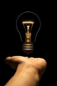 Hand holding a filament lamp on a black background. The bulb as a symbol of an idea. Glowing tungsten bulb. Ecological concept.