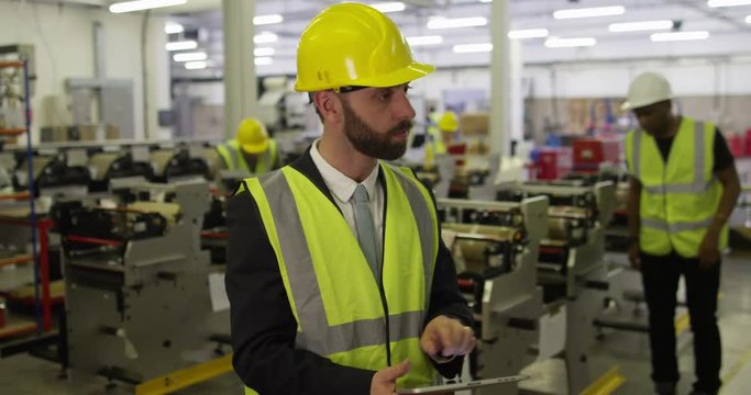 Manager at a shipping warehouse checks stock levels and inventory on a digital tablet.