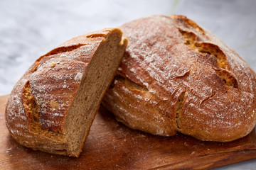 Fresh rye bread loaf on a wooden chopping board over white textured background, shallow depth of field