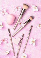 Obraz na płótnie Canvas Set of makeup brushes on pink background. Makeup cosmetic, beauty blender, silicone sponge and a beautiful spring flowers. Top view point, flat lay.