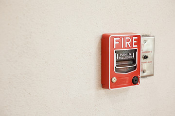 Red Fire alarm pull station switch install on white cement wall.