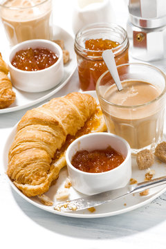 croissants with jam and coffee with milk for breakfast on white table, vertical