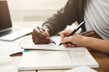 Male and female students at wooden table full of books