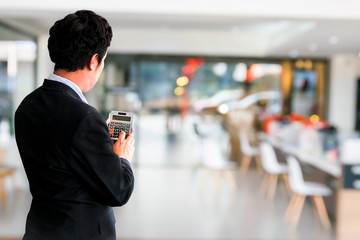 Asian man pressing calculator for business finance on car showroom blurry background.