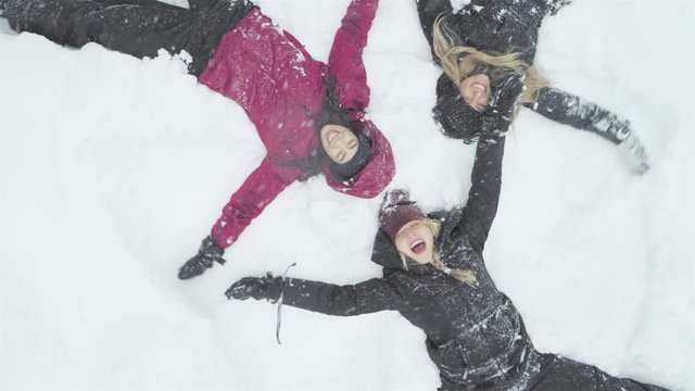 Three young beautiful women laying on the snow, and making snow angels