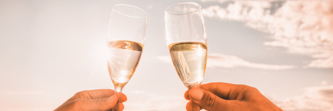 Couple toasting wine glasses for celebration. Champagne toast in luxury restaurant. Two people holding flutes doing cheers. Banner panorama crop on sunset background.