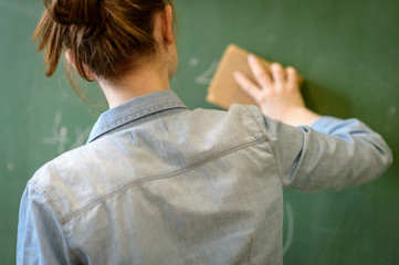 Female teacher or a student cleaning blackboard with a sponge. Rear view.