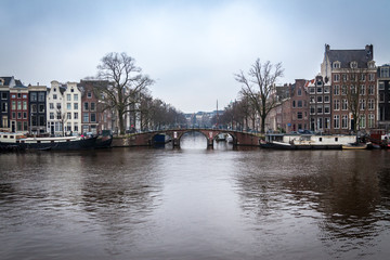 Fototapeta na wymiar water canals in Amsterdam with a bridge in the middle and buildings on both of bridge's side 
