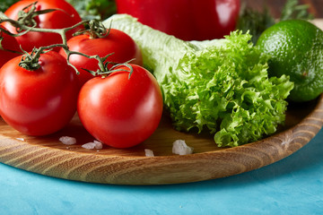 Still life of fresh organic vegetables on wooden plate over blue background, selective focus, close-up