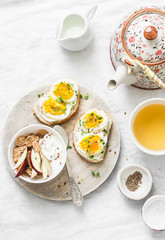 Morning breakfast table inspiration - sandwiches with cream cheese and boiled egg, yogurt with apple and flax seeds, herbal detox tea on light background, top view. Flat lay