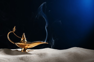Aladdin magic lamp on sand against dark background