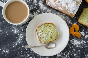 Mint cake sprinkled with powdered sugar on dark surface with fresh oranges mandarins