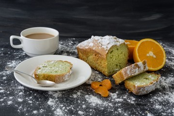 Mint cake sprinkled with powdered sugar on dark surface with fresh oranges mandarins