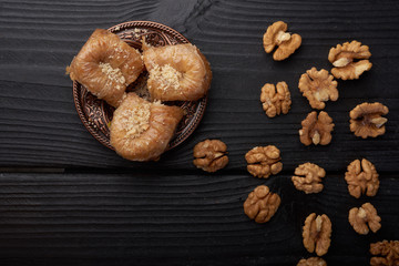 Turkish baklava near walnuts on black wooden background