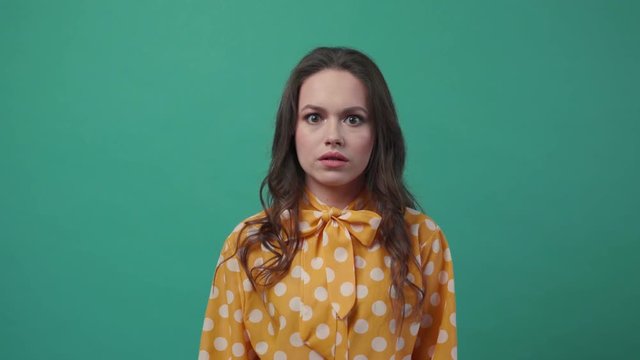 Nervous young woman in a colorful blouse gives an offended look straight to camera, stares wide-eyed, slaps her forehead, shakes her head. To be at a loss, conflict, troubles. Slow motion