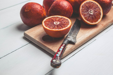 Blood oranges on a chopping board and a knife on a white wooden background. Seasonal citrus fruit