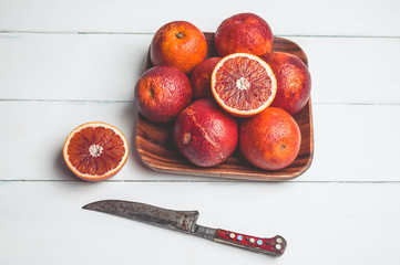 Blood oranges on a square plate and a knife on a white wooden background. Seasonal citrus fruit