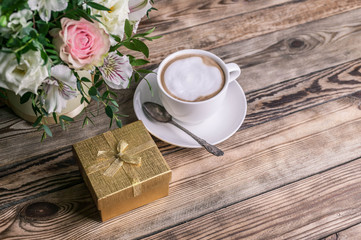 Fototapeta na wymiar Gift in a gold box, coffee latte in a white cup and a bouquet of flowers on a wooden table