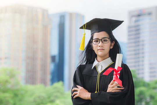 Happy graduate young Asian woman in cap and gown holding certificated in hand, Education concept