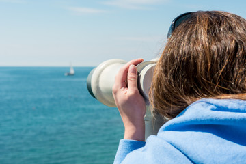 Woman looking through coin operated binoculars at seaside.