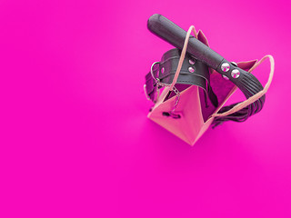 A leather whip and a collar with clamps are on a paper shopping bag. Background suitable for sex shop advertising