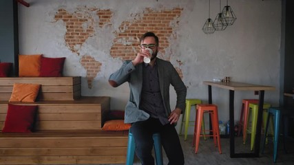 Portrait of successful Businessman entrepreneur working at busy office smiling. Fashionable modern young man with beard businessman smiling. It is located in modern office in loft style. Drinks cofee