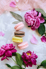 Spring composition flatlay: colorful macaroons with purple and pink peonies, green leaves on a light concrete background and a pink cloth