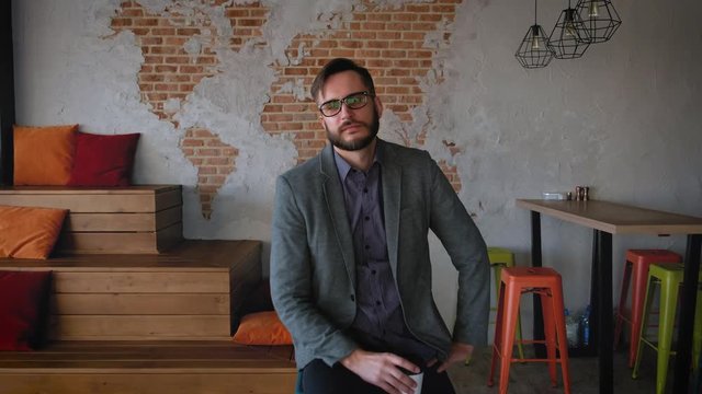 Portrait of successful Businessman entrepreneur working at busy office smiling. Fashionable modern young man with beard businessman smiling. It is located in modern office in loft style. Drinks cofee