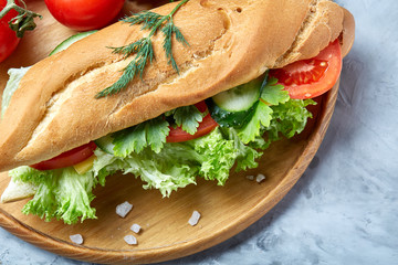 Fresh sandwich with lettuce, tomatoes and cheese served on wooden plate over white textured background, selective focus