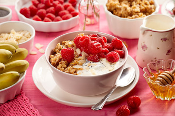 Granola with natural yogurt, fresh raspberries, honey, almond flakes, and poppy seeds in a ceramic bowl on a pink wooden table.  Delicious and nutritious breakfast or dessert. Healthy food.,