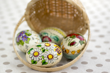 Group of wax painted Easter eggs spilled from light brown wicker baskets, flower ornaments, traditional decoration