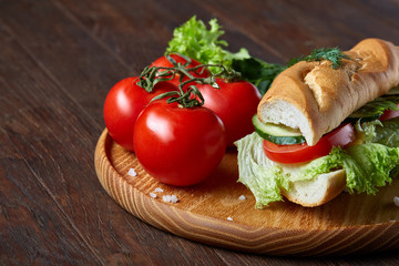 Fresh sandwich with lettuce, tomatoes and cheese served on wooden plate over wooden background, selective focus