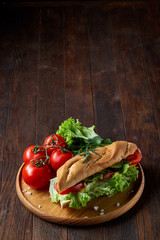 Fresh sandwich with lettuce, tomatoes and cheese served on wooden plate over wooden background, selective focus
