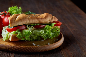Fresh sandwich with lettuce, tomatoes and cheese served on wooden plate over wooden background, selective focus