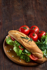 Fresh sandwich with lettuce, tomatoes and cheese served on wooden plate over wooden background, selective focus