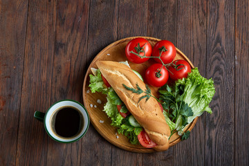 Fresh sandwich with lettuce, tomatoes, cheese on wooden plate, cup of coffee on wooden background, selective focus