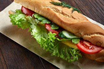 Fresh and tasty sandwich with cheese and vegetables on paper napkin over wooden background, selective focus, top view
