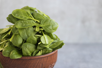 Fresh green spinach in brown bowl on gray background.