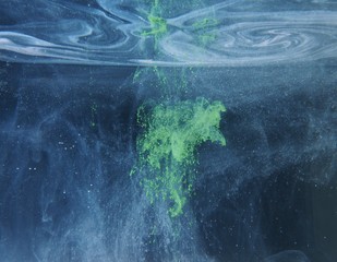 A drop of green paint dissolves in water. An abstract photo.