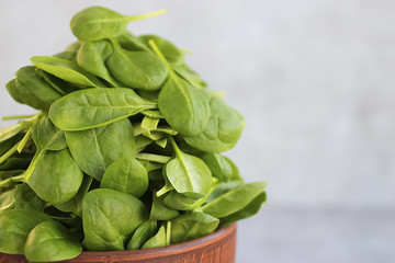 Fresh green spinach in brown bowl on gray background.