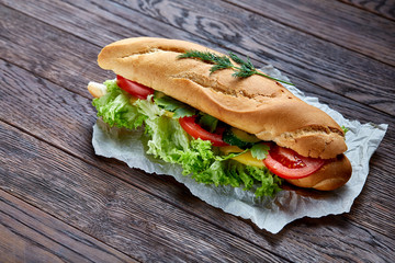Fresh and tasty sandwich with cheese and vegetables on paper napkin over wooden background, selective focus, top view