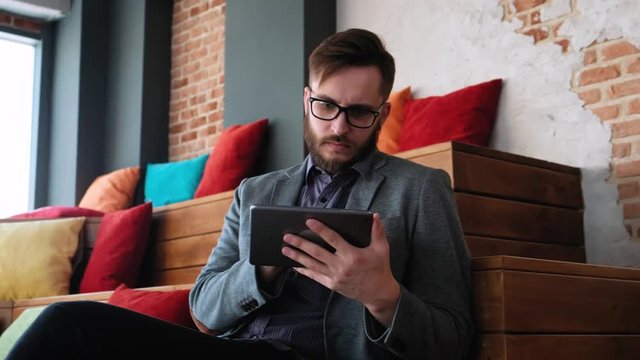 Attractive young man with digital tablet in soft natural light. A fashionable modern young man with a beard uses a tablet in a modern office in loft style.